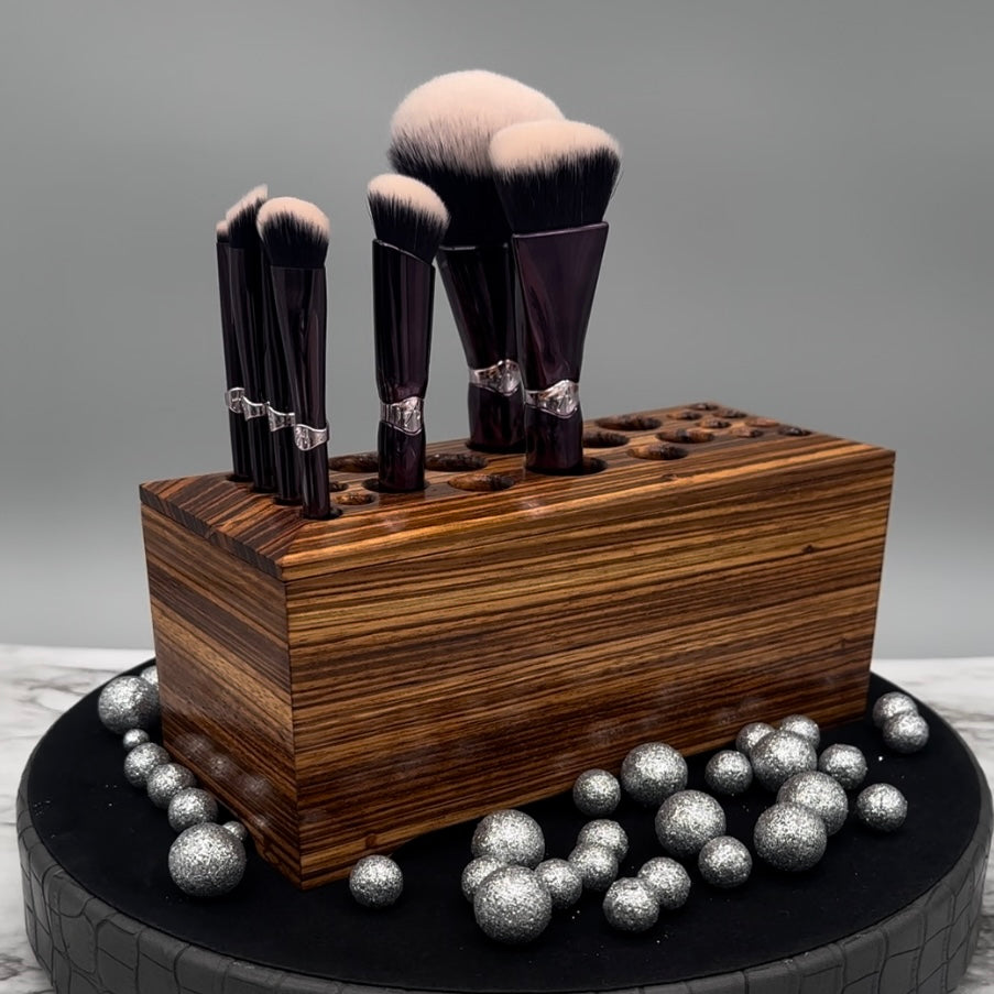 Makeup brushes in a Zebrawood wooden holder with decorative silver balls on a gray background